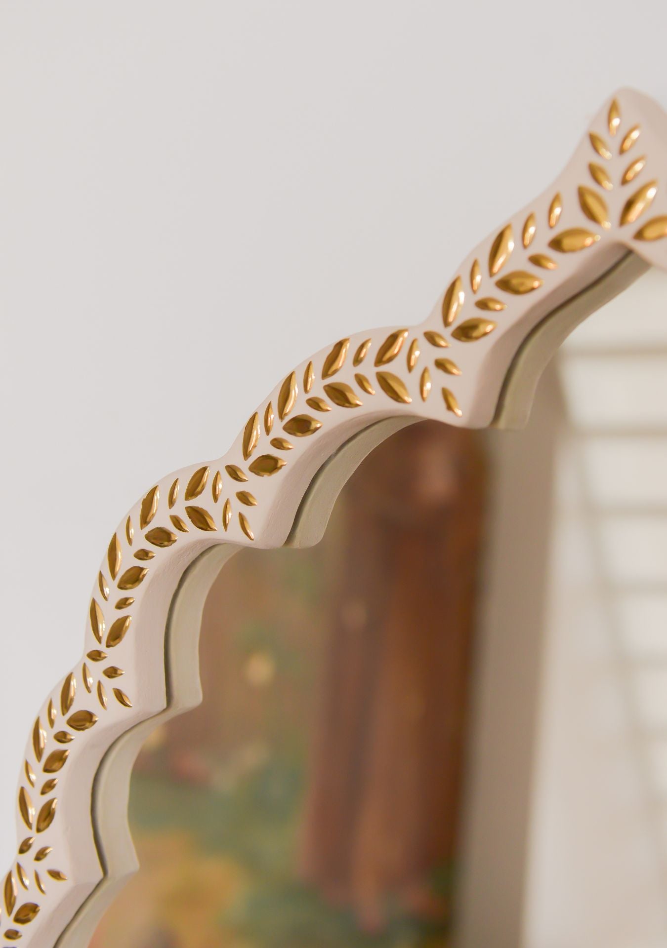Upper edge detail of handcrafted mirror with golden mosaic leaf design and curved oriental shape – Pure Reflection.
