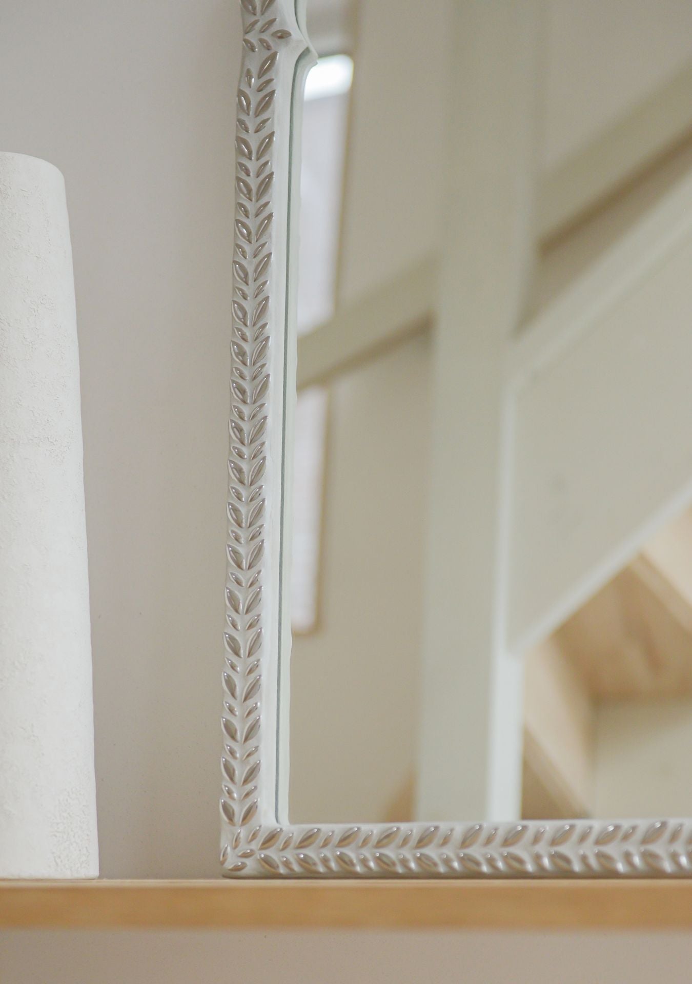 Detail of a handcrafted mirror with silver mosaic leaf design, reflecting a calm neutral staircase interior – Pure Reflection.