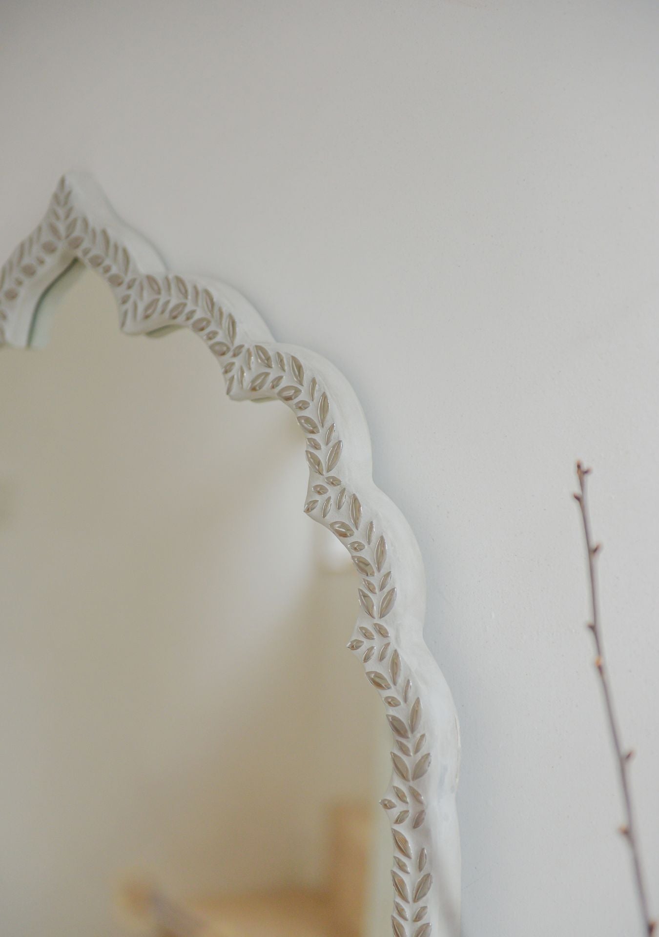 Close-up of the upper edge of a handcrafted mirror with silver mosaic leaf pattern and soft curved silhouette – Pure Reflection.