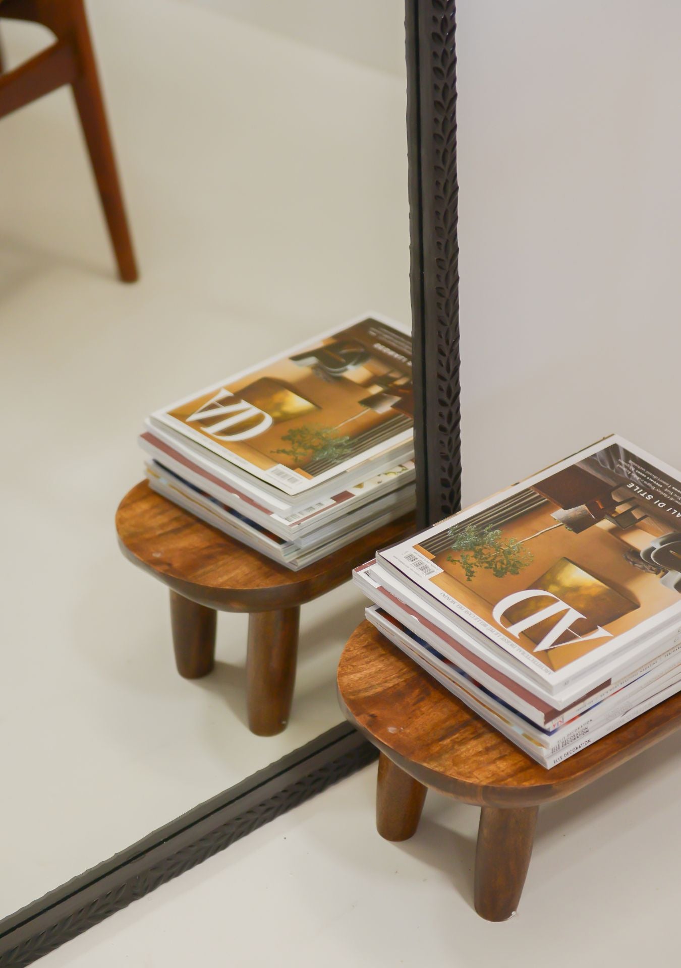 Close-up of handcrafted black mosaic mirror reflecting wooden table with design magazines.
