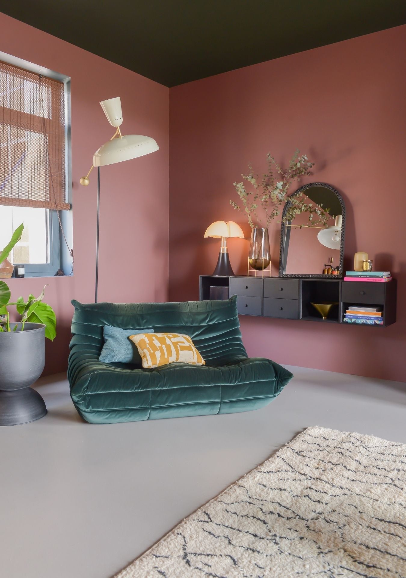 Handmade mosaic mirror by Pure Reflection styled in a warm, modern living space with a colorful wall, black floating cabinet, and green velvet lounge chair for a cozy, elegant look.