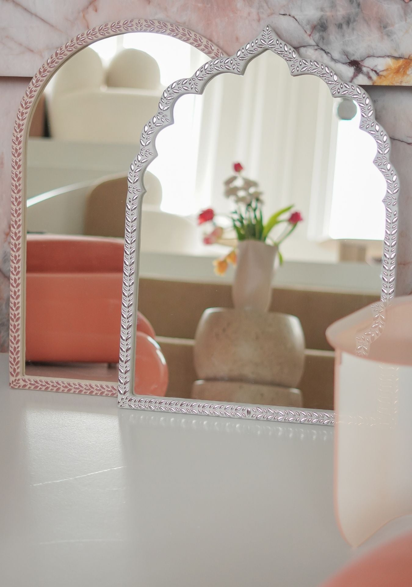 Two handmade mosaic mirrors by Pure Reflection, one with a soft arch and one with an oriental arch shape, both featuring a delicate pink leaf-patterned frame and styled in a warm, modern interior with natural light and sculptural decor.
