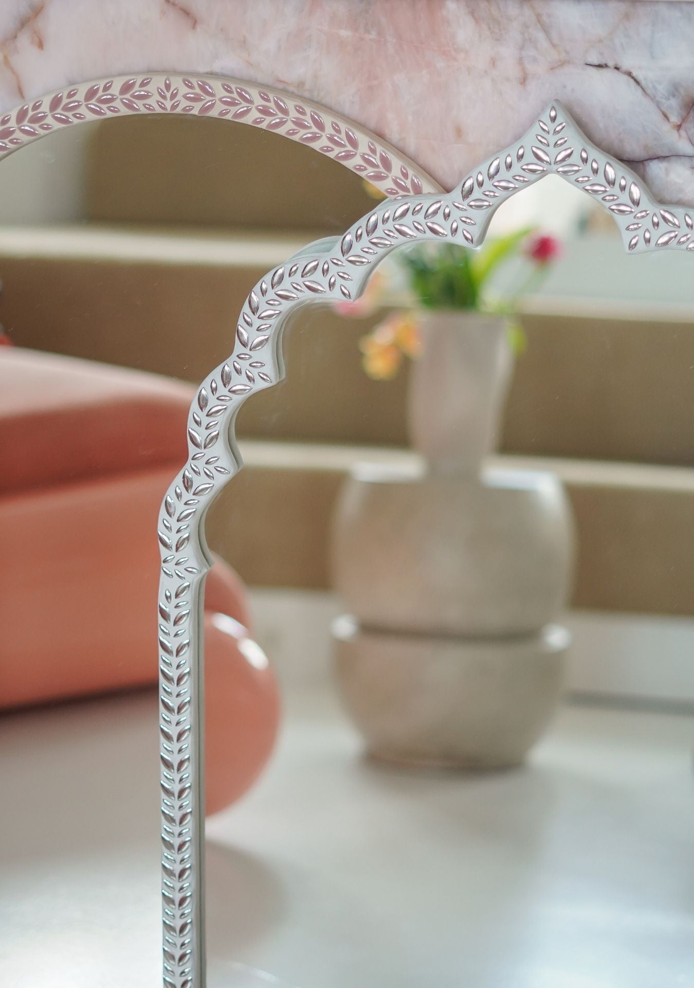 Detail of a handcrafted mirror with silver mosaic leaf design and curved oriental frame, styled with ceramic vases in soft earthy tones – Pure Reflection.