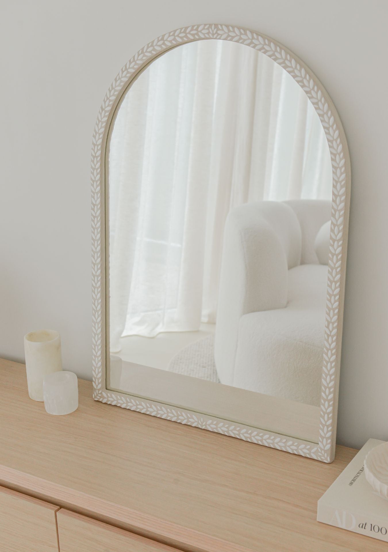 Handmade white arched mosaic mirror by Pure Reflection, styled in a bright minimal interior with neutral tones, soft natural light, and a light wooden cabinet for a calm, elegant look.
