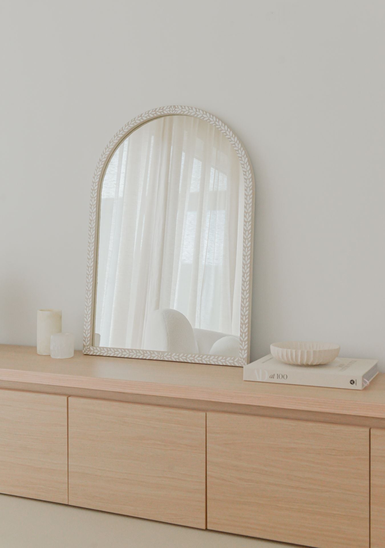 Handmade arched mosaic mirror by Pure Reflection styled in a bright, minimal interior with neutral tones, placed on a light wooden cabinet with soft natural light and serene decor.