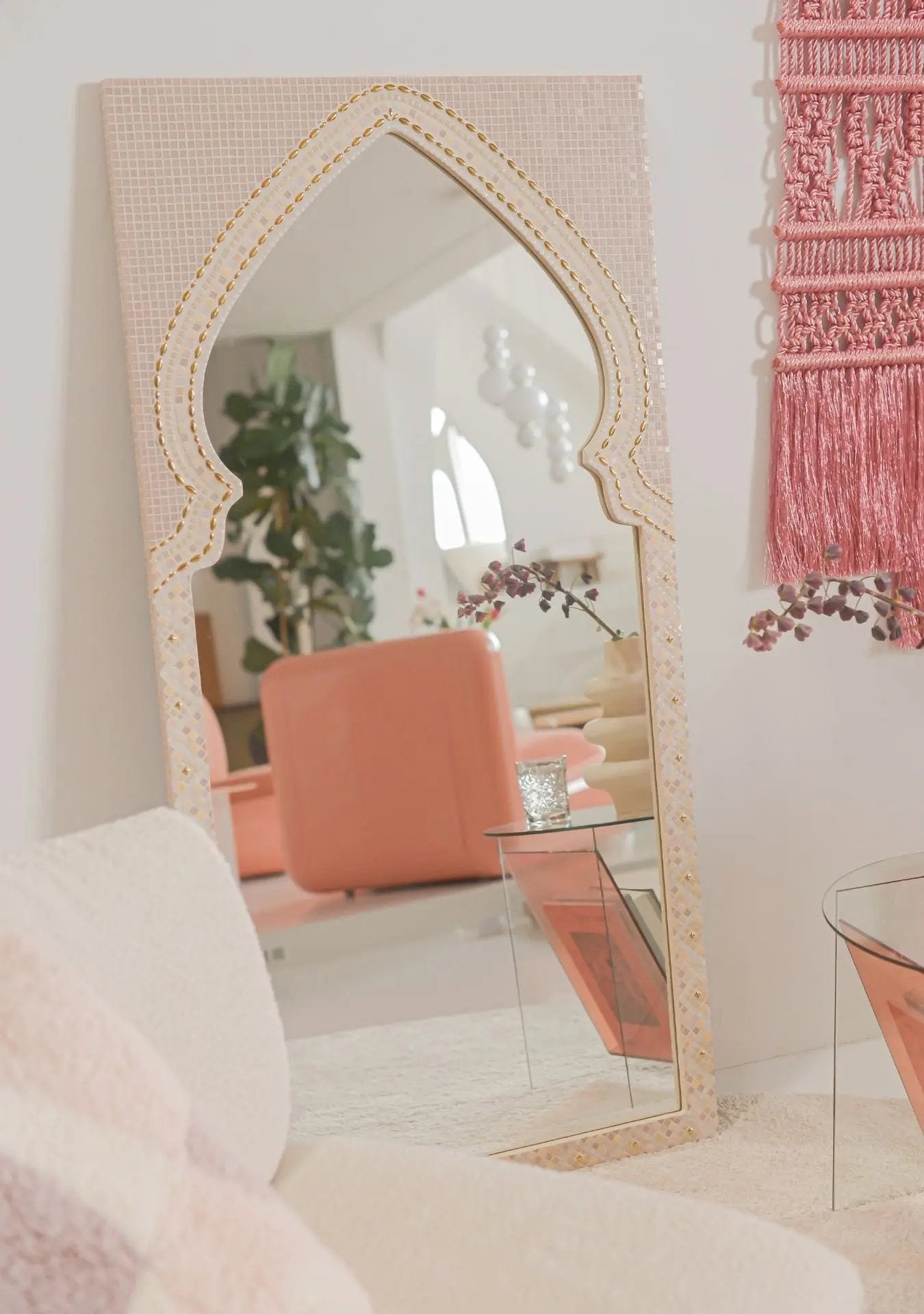 Elegant arched mosaic mirror with ceramic stones and blush details beside a boucle armchair.