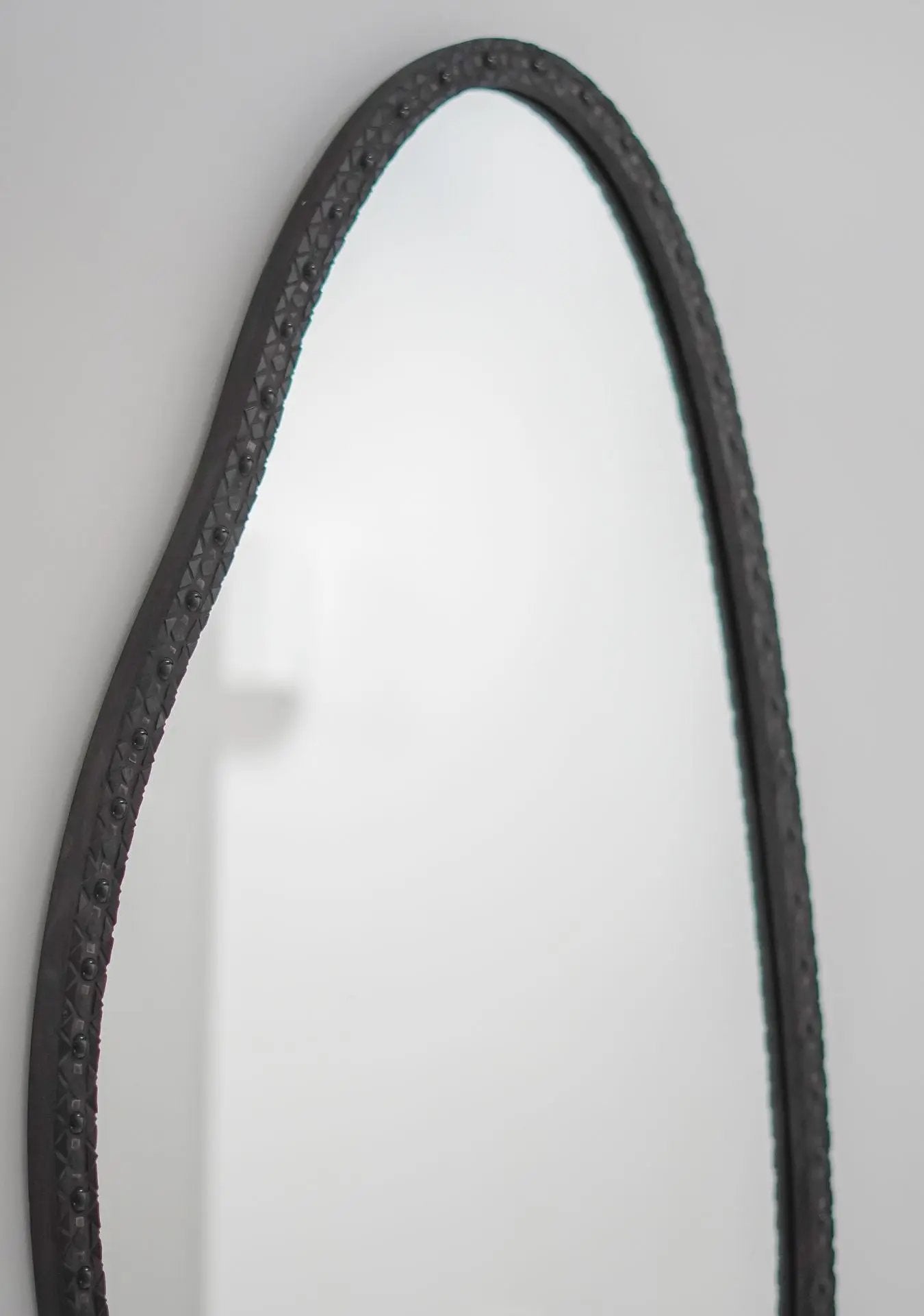 Artisan-made black oval mirror reflecting calm and timeless sophistication.