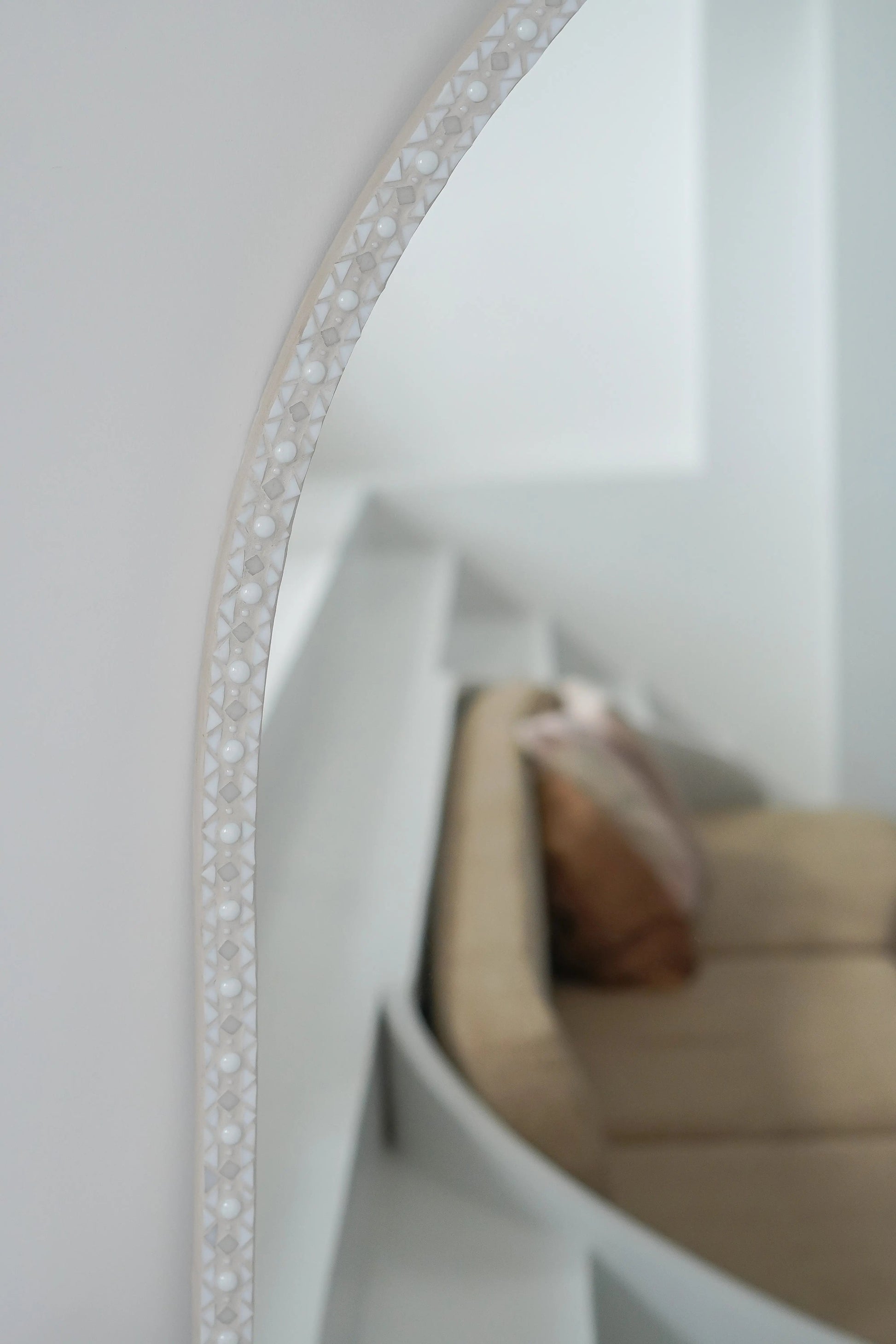 Elegant oval mirror reflecting light and natural textures in a serene space.